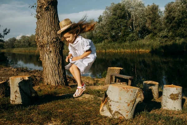 Enfant fille joue et saute d'un moignon sur fond de rivière . — Photo