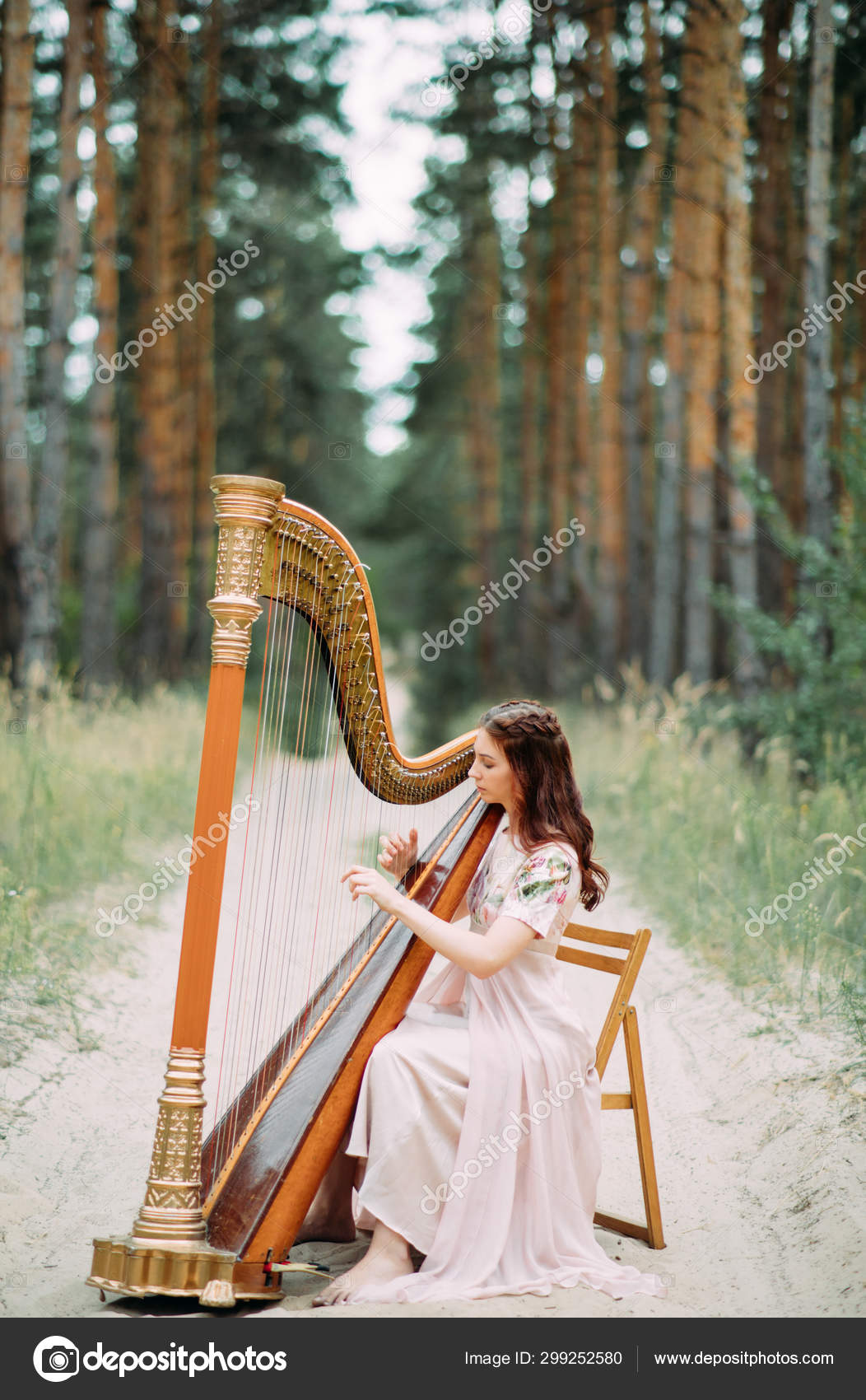 Mulher harpista senta-se na floresta e toca harpa contra um fundo fotos,  imagens de © stasia04 #299252580