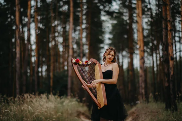 Mujer arpista camina en el bosque y toca el arpa contra un fondo — Foto de Stock