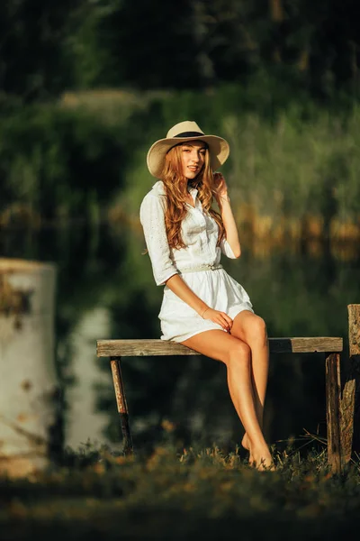 Mujer joven y bonita está sentada en el banco junto al río . —  Fotos de Stock