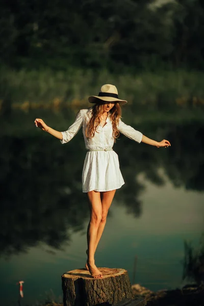 Mujer bonita está de pie en el tocón del árbol al lado del río . —  Fotos de Stock