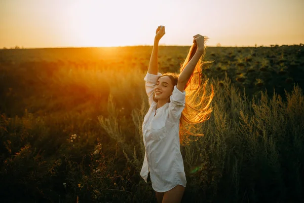 Ευτυχισμένη χαρούμενη γυναίκα περπατάει στο λιβάδι το ηλιοβασίλεμα. — Φωτογραφία Αρχείου