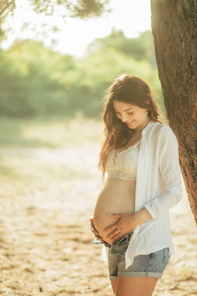 Boldog terhes nő az erdőben a fa mellett. — Stock Fotó