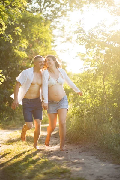Dvojice s těhotnou ženou se baví a běhá v lese. — Stock fotografie