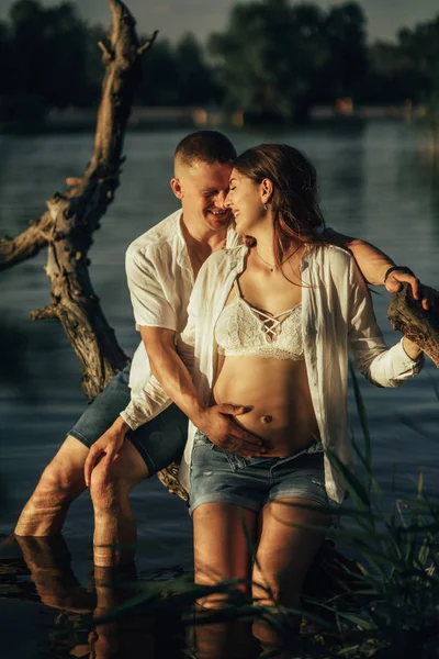 Пара с беременной женщиной смеется сидя на загвозде среди реки . — стоковое фото