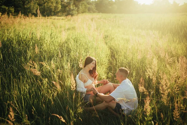 妊娠中の女性との幸せなカップルは、草の間の草原に座っています. — ストック写真