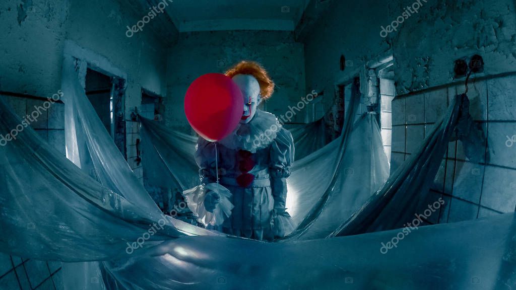 A clown with red balloon stands in old abandoned building. A clown with red balloon stands in old abandoned building.