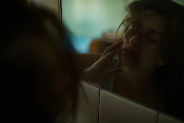 Pobity zakrwawione kobieta ofiara przemocy bada jej rany twarzy w lustro. — Zdjęcie stockowe