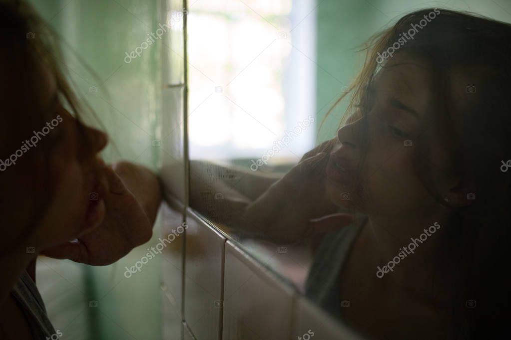 Beaten bloodied woman victim of violence examines her facial wounds in the mirror. 
