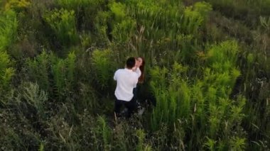 İnsansız hava aracından mutlu genç aileye güzel bir manzara çayırda bebekle oynuyor..