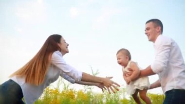 Mutlu, genç bir aile çayırdaki çiçeklerin arasında bebekle oynuyor..