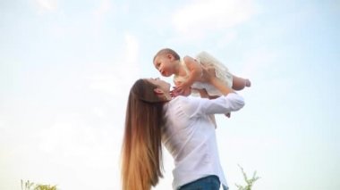 Mutlu genç aile bebekle oynuyor ve onu çayırdaki çiçeklerin arasında öpüyor..
