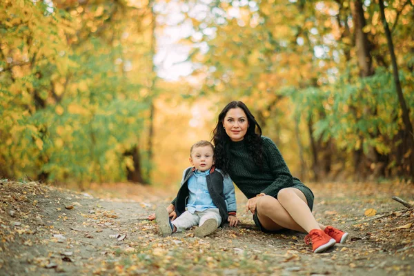 Uma mãe e um filho sentam-se em um caminho na floresta de outono . — Fotografia de Stock