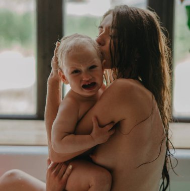 Anne küvette banyo yapar ve ağlayan bebeğini teselli eder. Yakın çekim..
