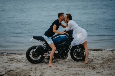 Sahilde sevişen bir çift, motosikletin üstünde su üstünde oturuyor..