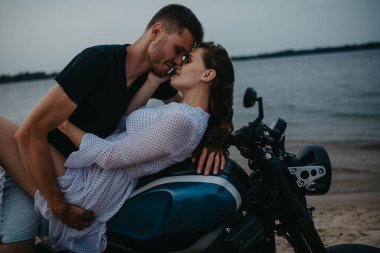 Çift plajda sevişiyor, motorsikletin üstünde su üstünde yatıyor. Yakın çekim..