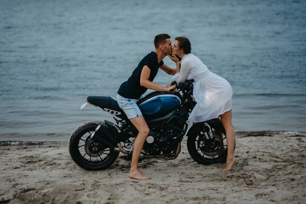在沙滩上相亲相爱的情侣坐在摩托车上 背靠水 — 图库照片