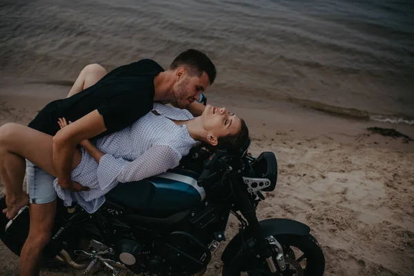 Couple makes love on beach lying on motorcycle on water background.