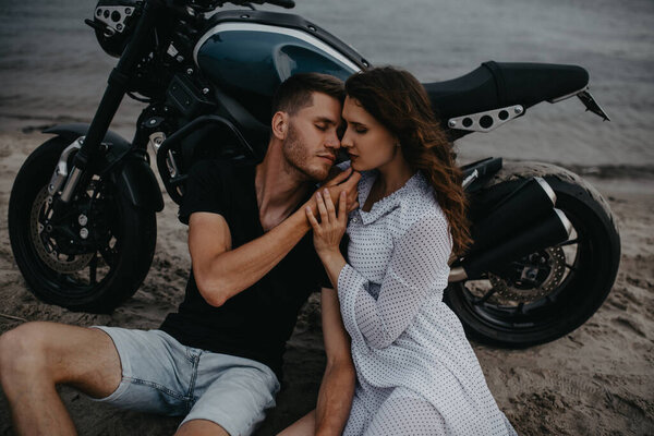 Couple in love sits and hugs on sandy beach near motorcycle. Closeup. Top view.