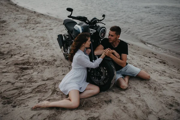 愛のカップルは座って オートバイの近くの砂浜で互いに手を取り合っています トップ表示 — ストック写真