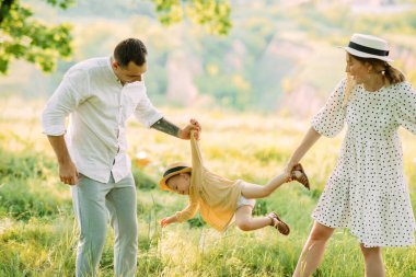 Genç ebeveynler parkta yürürken eğlenip kızlarıyla oynuyorlar..