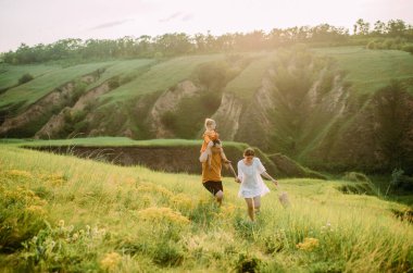 Küçük kızı olan genç bir aile eğleniyor, koşuyor ve neşeyle gülüyor..