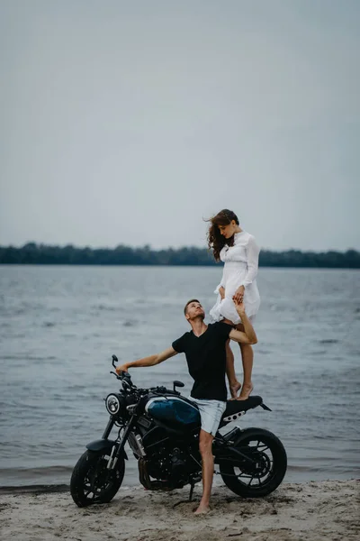 恋のカップルは水の背景にオートバイの近くのビーチにあります — ストック写真