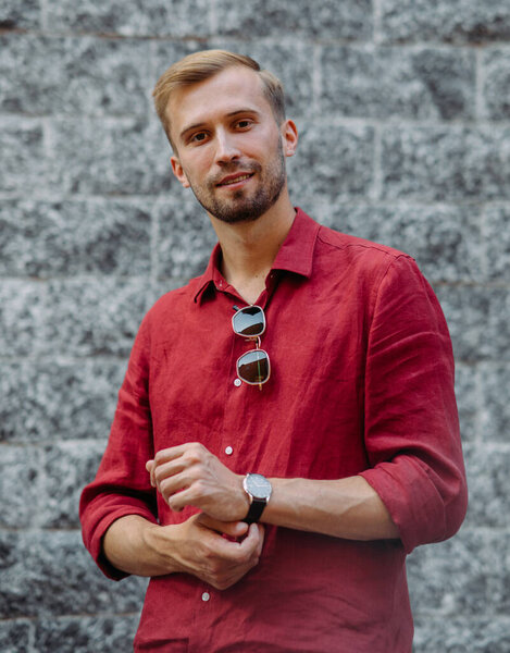 Portrait of young man in red shirt with sunglasses against background of grey brick wall.