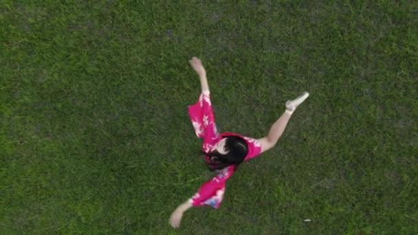 赤い着物の日本のバレリーナは 芝生の上で踊りの要素を繰り返します トップ表示 — ストック動画