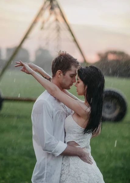 恋に溺れたカップルが立って 日没時に農業の噴霧器から水滴の下に包含します — ストック写真