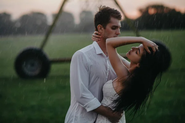 坠入爱河的情侣们站在那里 在夕阳西下拥抱在农用喷雾器的水滴下 — 图库照片