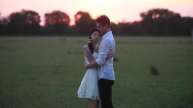 Aşık bir çift gün batımında çayırda durur ve kucaklaşır..