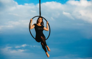 Kadın akrobatik elementler sergiliyor mavi gökyüzü ve beyaz bulutların arka planında asılı duran hava çemberinde.