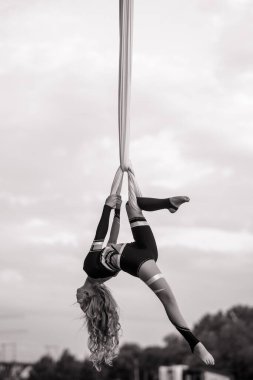 Çocuk akrobatik hareketler yapan akrobatik kız gökyüzü ve ağaçların arka planına havadan ipek asıyor. Siyah ve beyaz resim.