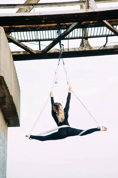 在天空的背景下 女空想家在连接在舰桥支撑物上的悬挂的空中丝上表演体操分裂 — 图库照片