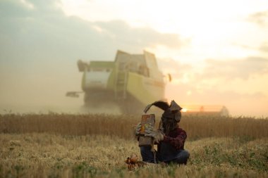 Şapkalı, tavşan kulaklı büyücü imajı olan bir adam buğday tarlalarının arasında oyuncak bebeğin yanında oturur ve eski oyuncak arabayı elinde tutarak gün batımına ve hasatçıya karşı sihirli bir ayin yapar..