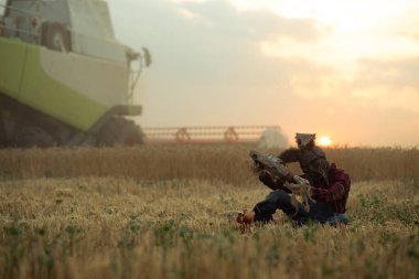 Şapkalı, tavşan kulaklı büyücü imajı olan bir adam buğday tarlalarının arasında oyuncak bebeğin yanında oturur ve eski oyuncak arabayı elinde tutarak gün batımına ve hasatçıya karşı sihirli bir ayin yapar..