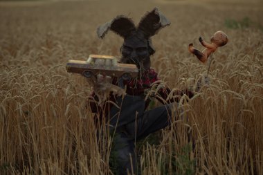 Tavşan kulaklı büyücü imajı takmış bir adam bir vudu ritüeli gerçekleştiriyor ve akşamları oyuncak tel ve eski oyuncak arabayı buğday tarlasında tutuyor..