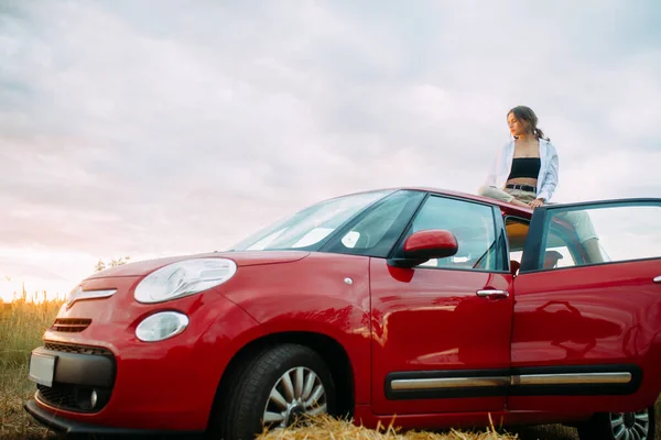 Jonge Vrouw Zit Rode Auto Dak Ontspant Weide Avond — Stockfoto