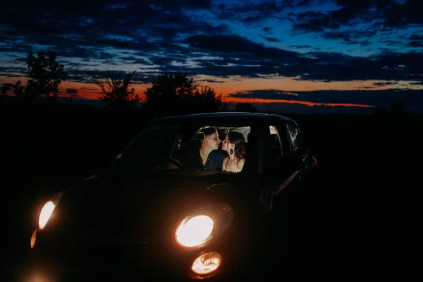 Ungt Par Kærlighed Sidder Inde Bilen Med Glødende Forlygter Kys - Stock-foto