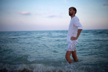 Genç düşünceli adam sahilde suda duruyor. Akşamları deniz ve gökyüzüne karşı..