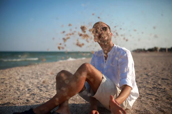 Joven Gafas Sol Sienta Playa Divierte Ríe Arroja Arena Contra — Foto de Stock