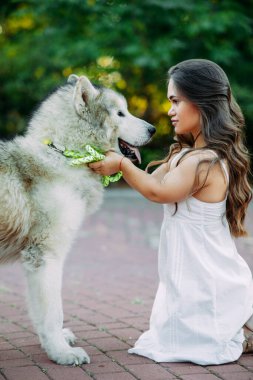Doğuştan hastalıklı genç bir kadın parkta yürürken Malamute köpeğini kucaklıyor..