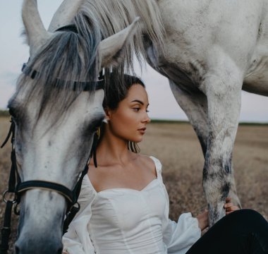 Genç düşünceli kadın ve çayırdaki gri atın portresi.