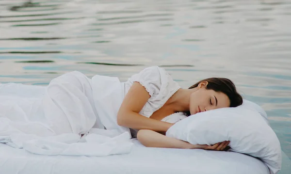 若い女性は白い寝具と水の中に浮かぶマットレスの上で眠る — ストック写真