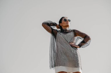 Güneş gözlüklü güzel kadın gri gökyüzünün arka planında poz veriyor..