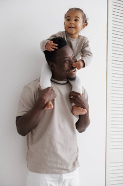 Mutlu baba, sevimli melez kızını omuzlarında taşıyor, neşeli bir anı paylaşıyor. Irklar arası aile kavramı.