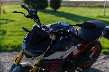 Yakın plan, modern kırmızı ve siyah motosikletin ön ve gidonlarının yüksek açılı görüntüsü, yumuşak odaklı yeşil park arka planına göre ayarlı..