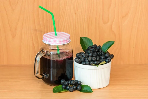 Chokeberry 或黑楸楸汁与冰在玻璃与稻草和浆果在篮子附近在木背景 免版税图库照片