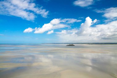 Düşük tide üzerinde İngilizce bir güneşli yaz gününde (La Mancha) Kanal. Güzel yaz manzara mavi gökyüzü ve beyaz bulutlar. Küçük bir ada ve arka planda yeşil bir plaj. Bulutların üstünde ıslak kum yansımasıdır. . Mont San Michel Abbey. N